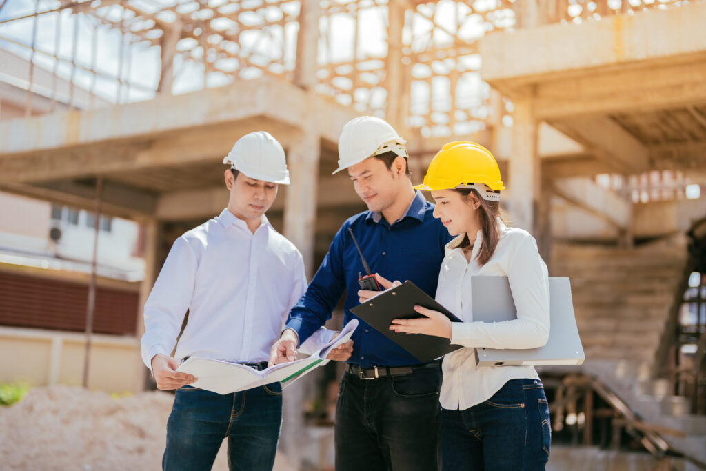 Team of 3 engineers man and woman design big business project about industrial architecture model design on construction site with blueprints, walkie talkie and listnotes wearing hard hats.
