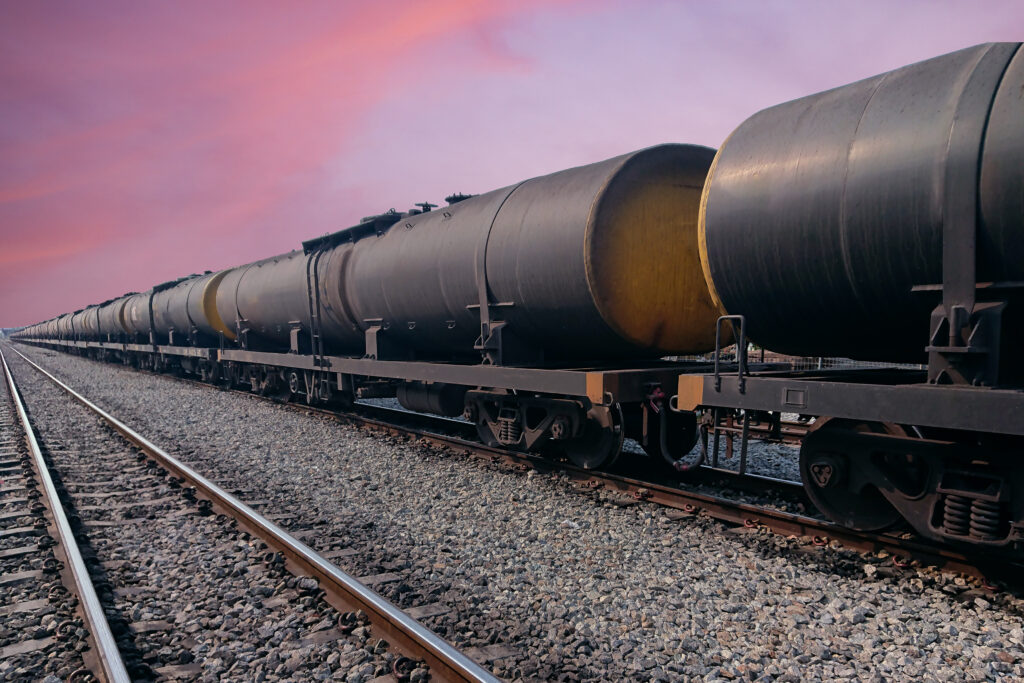 Black freight train wagons having oil tankers waiting on the rails againt sunrise sky